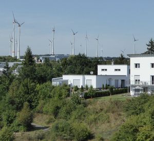 Das Bild zeigt ein Wohngebiet mit Windkraftanlagen im Hintergrund