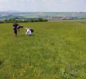 Das Foto zeigt zwei Studierende, die auf einer eröhten Wiese kartieren. Im Hintergrund sind Felder, Ortschaften und Windräder zu erkennen.