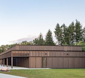Das Foto zeigt ein großes Holzgebäude am Waldrand.