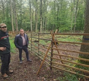 Das Bild zeigt zwei Männer vor einem Gatter im Wald